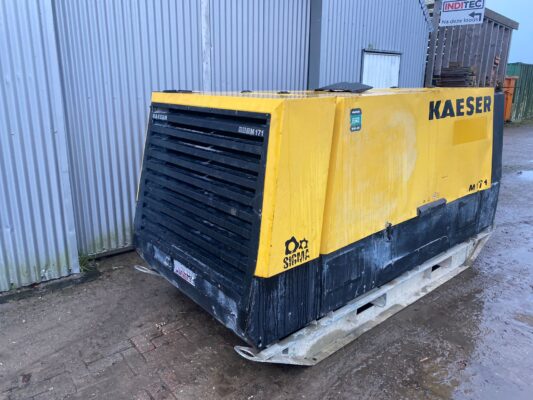 KAESER M171 mobiele luchtcompressor met een zwarte voorkant en gele behuizing, geplaatst op een modderige bouwplaats